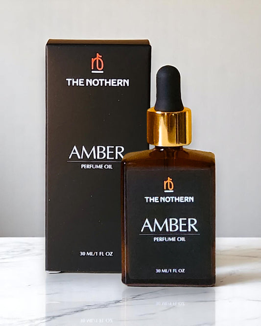 A bottle of 'The Nothern Amber Perfume Oil' with a dropper, placed in front of its packaging box on a marble surface.