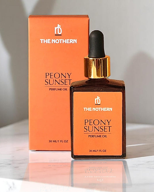 A bottle of Peony Sunset Perfume Oil by The Northern, with a dropper cap, next to its orange packaging box.