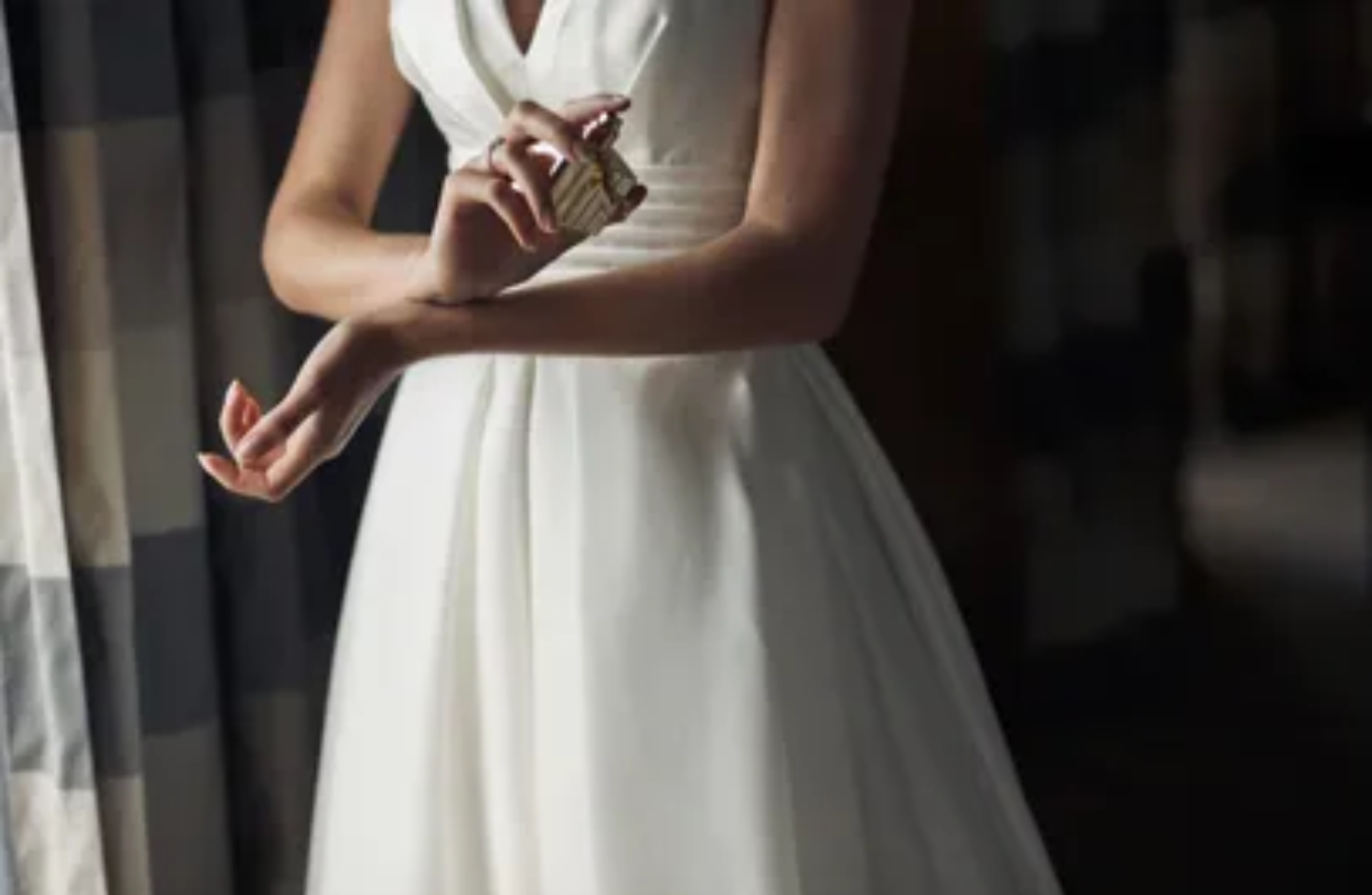 woman in white dress spraying perfume, mid section crop